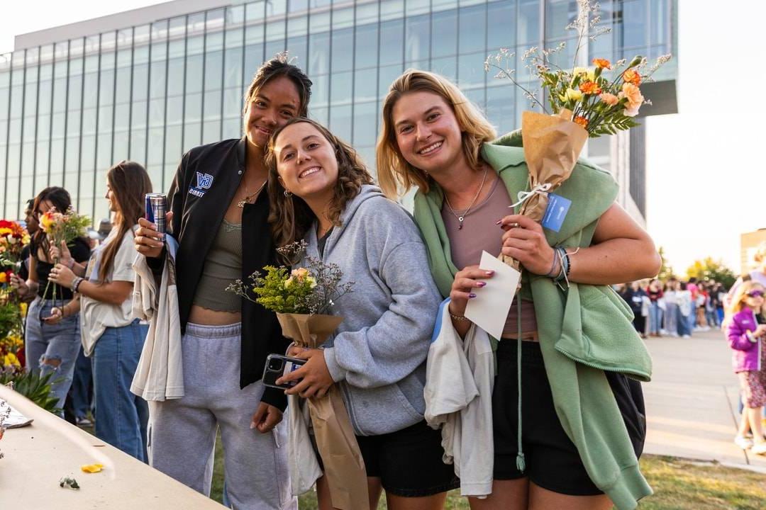 students smiling and holding flowers